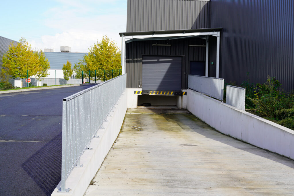 A declining loading dock with a sloped driveway at the edge of a warehouse in an industrial park.