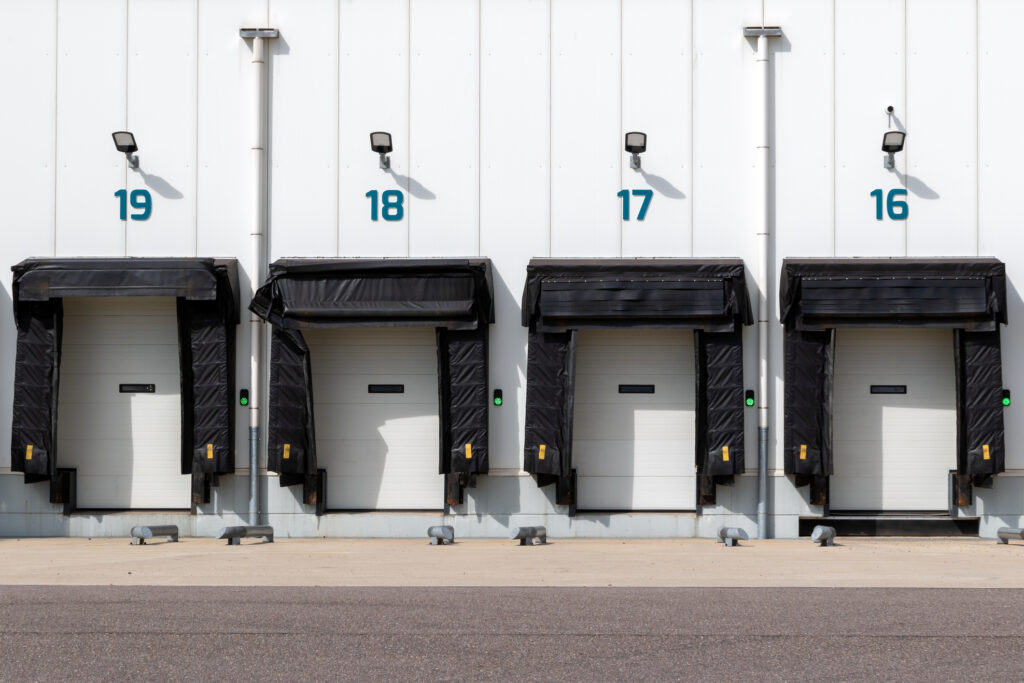Row of loading docks with shutter doors and dock shelters at an industrial warehouse.