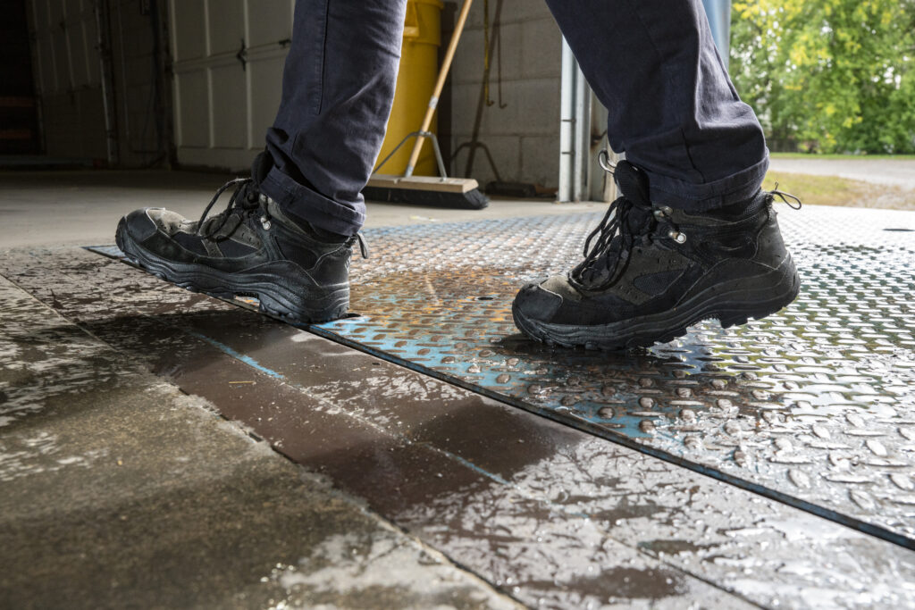 Close-up view of a warehouse worker’s feet in safety shoes as they walk on a wet tread plate on a loading dock.