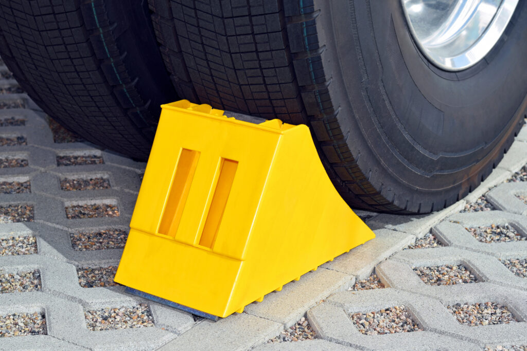 Close-up of a yellow wheel chock wedged at a truck’s tire.