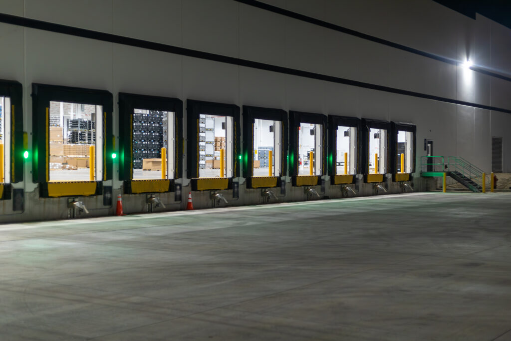 A series of eight open loading docks viewed from outdoors with green communication lights lit up beside each.