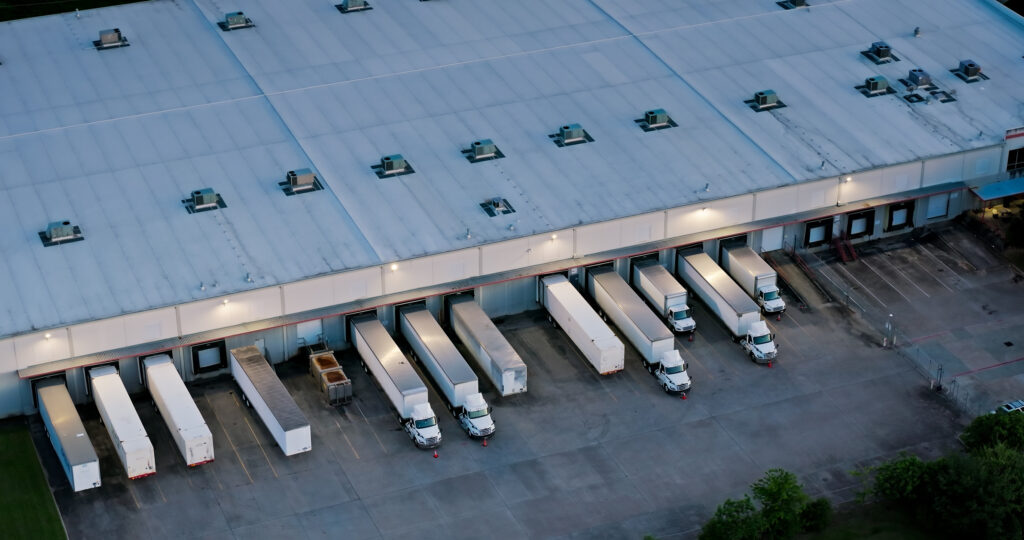 Aerial shot of large semi-trucks parked at their respective loading docks at a warehouse.